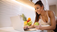 Fit smiling young woman with apple in modern kitchen