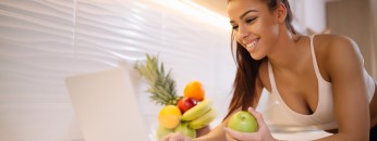 Fit smiling young woman with apple in modern kitchen
