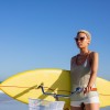 Front view of African american woman with surfboard sitting on bicycle at beach in the sunshine